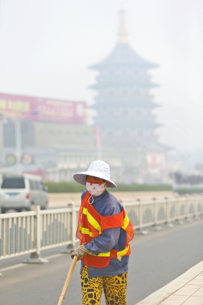 近日，在古都洛陽，環(huán)衛(wèi)工人身后的“天堂”被霧霾籠罩著。